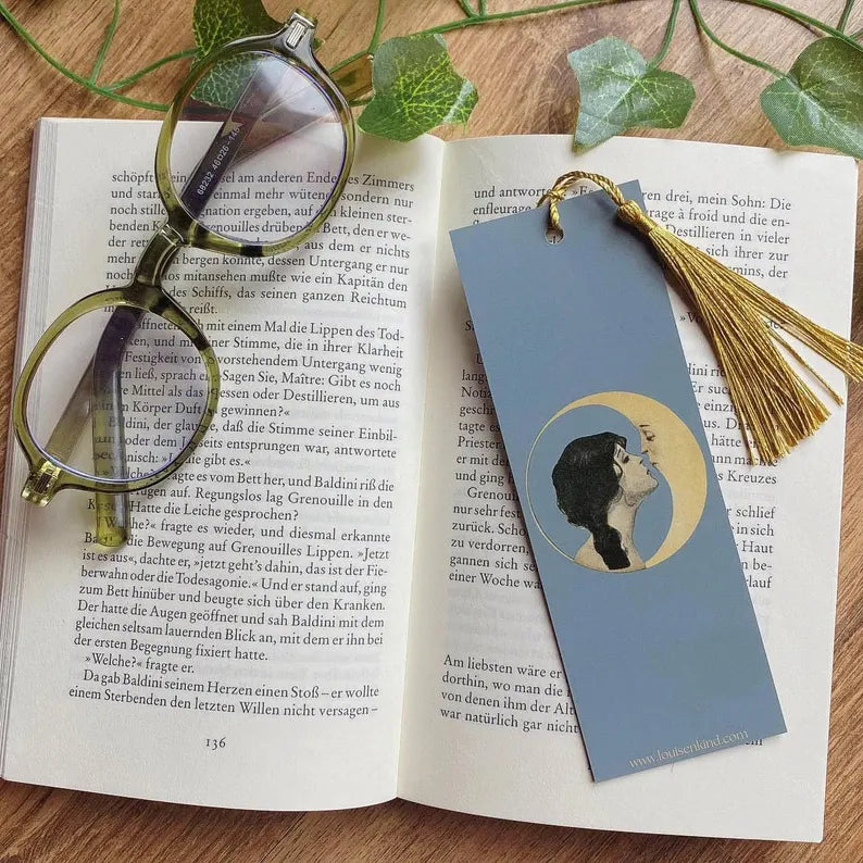 Aesthetic vintage moon bookmark with golden tassel and Green glasses laying on an open book