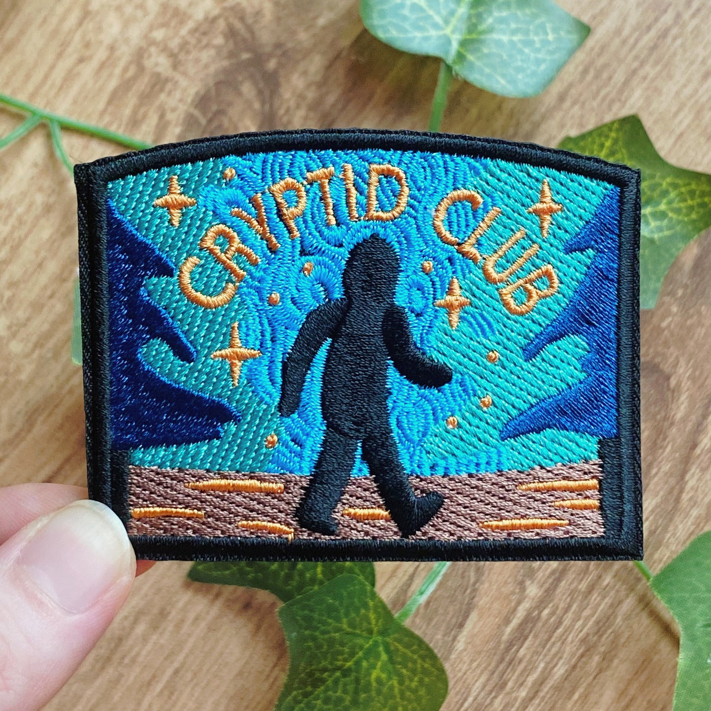Embroidered patch with 'Cryptid Club' text and Bigfoot silhouette on a blue background