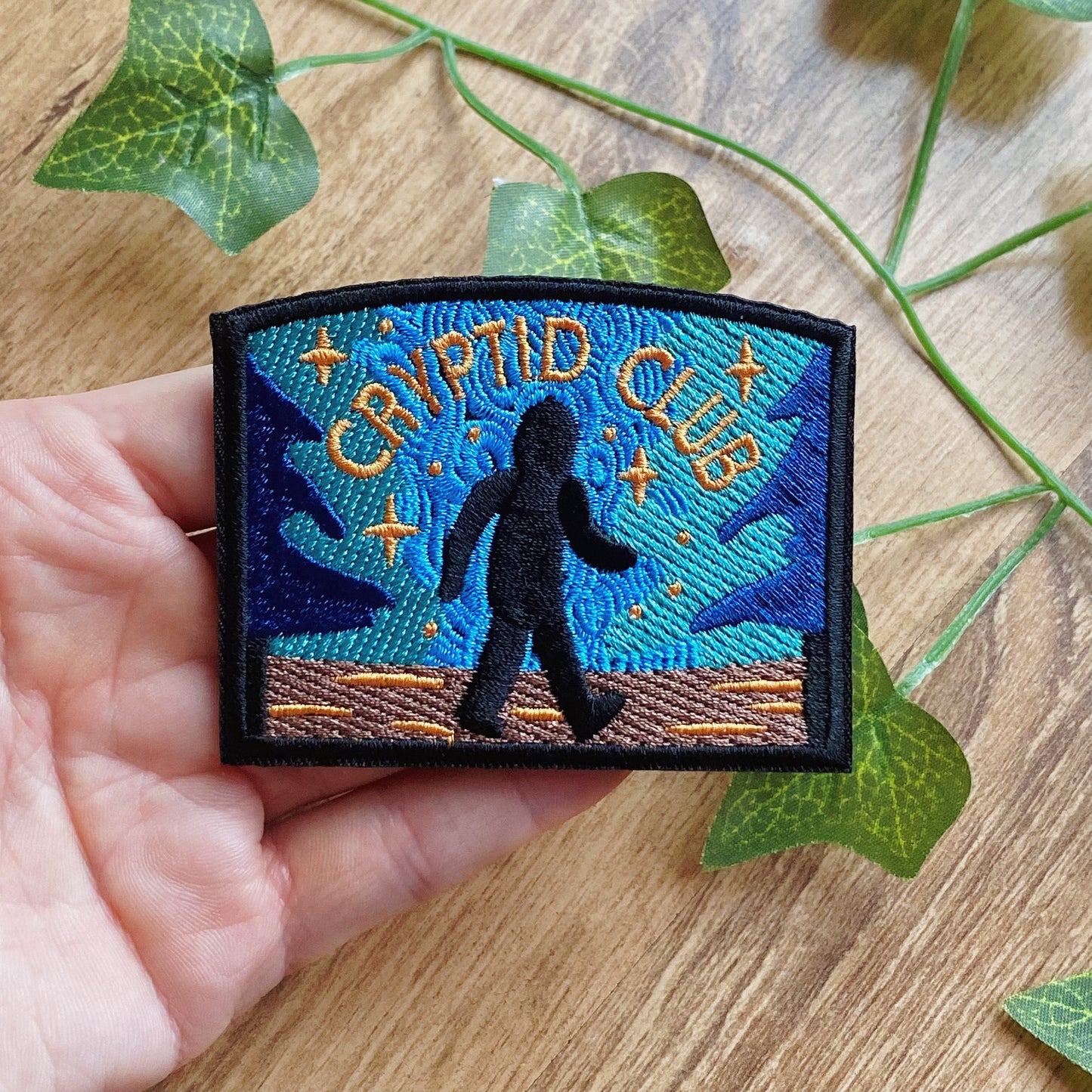 Embroidered patch with 'Cryptid Club' text and Bigfoot silhouette on a blue background