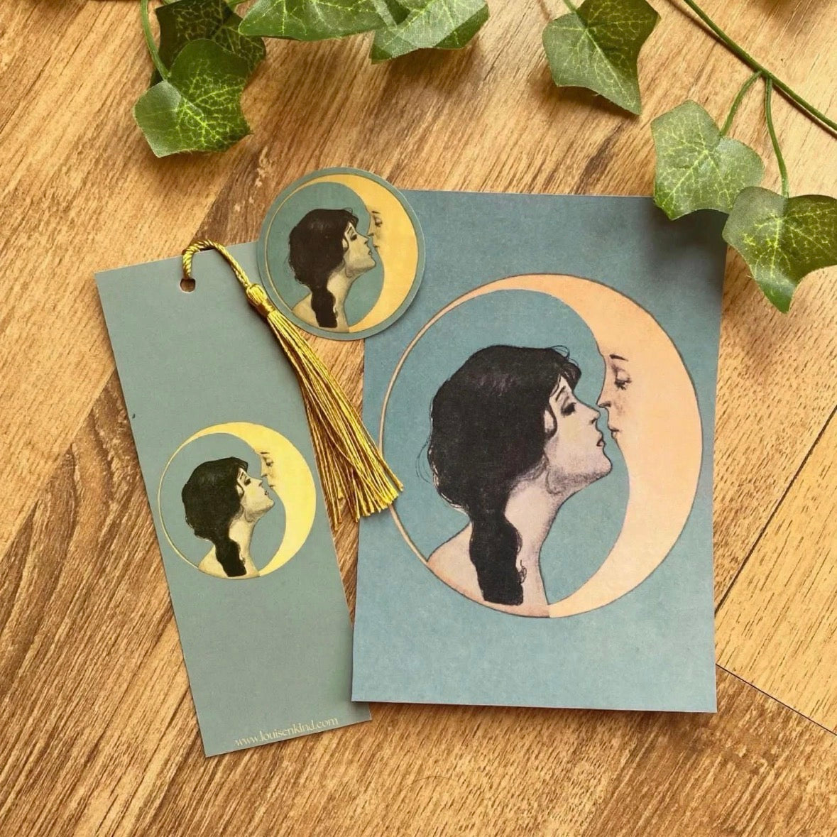 woman kissing moon gift set with postcard bookmark with gold tassel and round vinyl sticker vintage celestial art nouveau bundle on wooden table